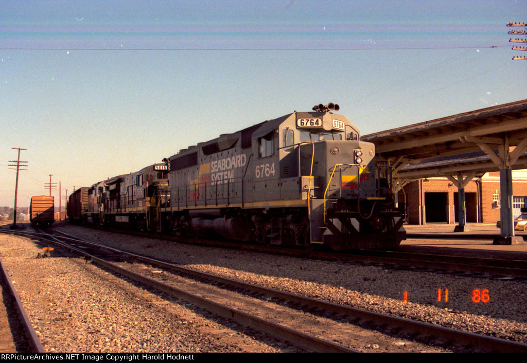 SBD 6764 leads a train past the station